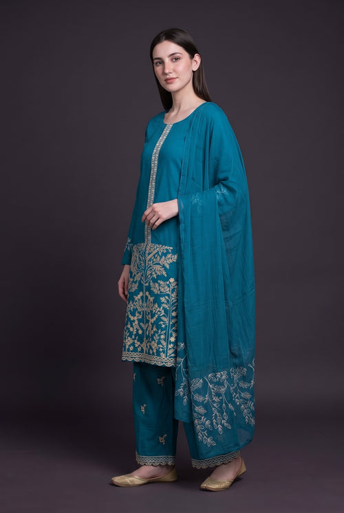 Model wearing the Blossom Tree Suit in peacock blue, showing the embroidered tree panel and trouser hem